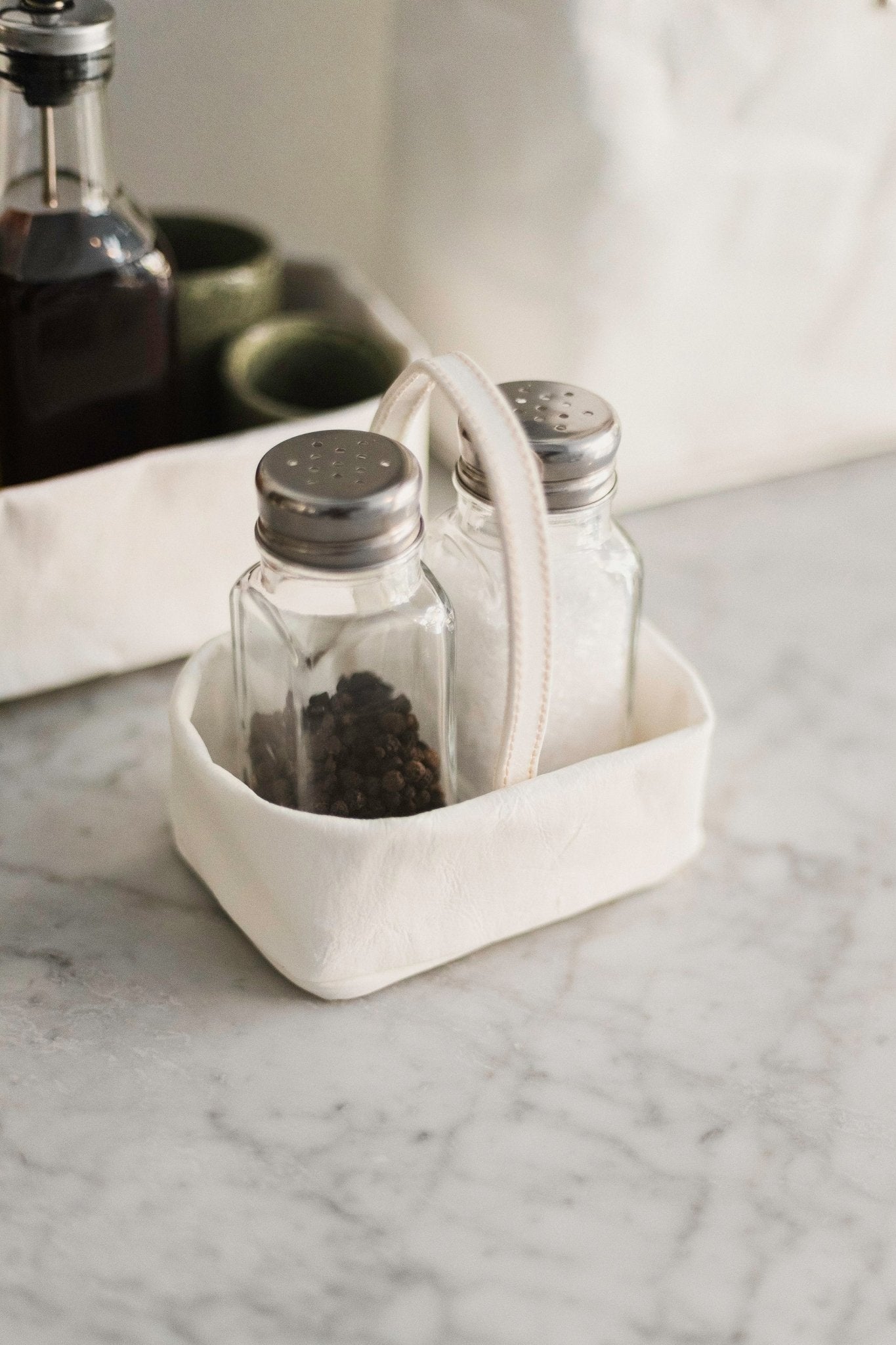 A small rectangular washable paper salt and pepper holder is shown with a washable paper small carry handle. The salt and pepper holder shown is white and is shown holding small glass salt and pepper shakers with metal lids.