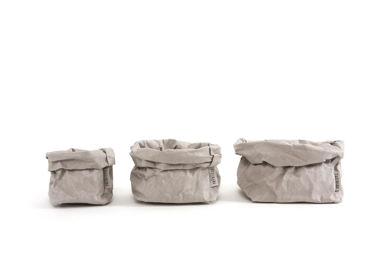 A small, medium and large paper bag in pale grey are lined up in size order from small to large.
