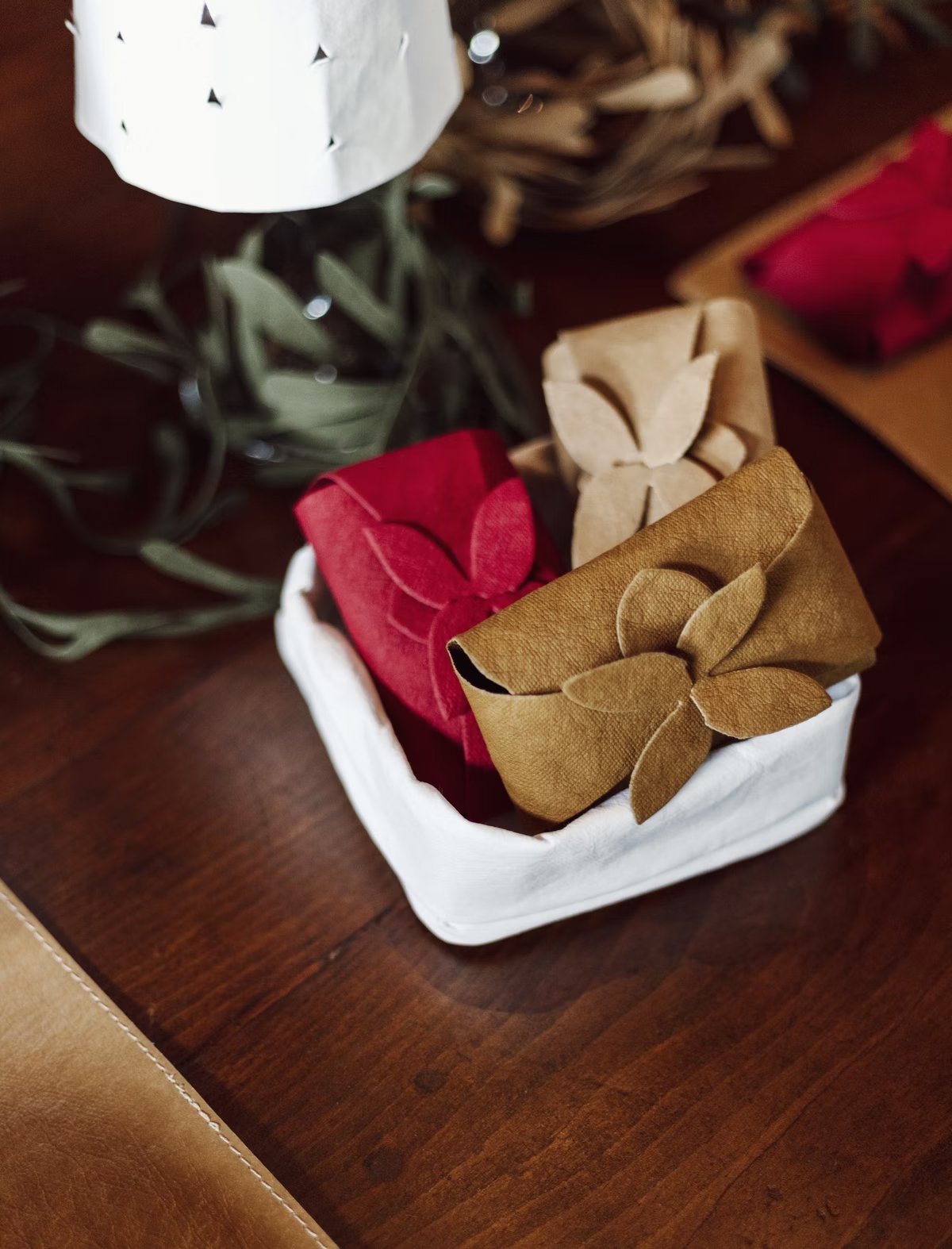 A washable paper tray is shown on a a wooden table. Inside the tray are three washable paper soap holders in red, tan and cream. The soap holders are shown closed with flower petal folded closures.