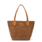 A small washable paper woven tote is shown. It has two long tan leather handles and a tan leather UASHMAMA logo label on the outside in between the handles. The bag shown is in a dark tan colour.
