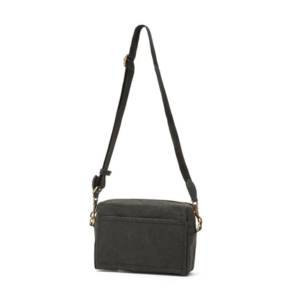 A rectangular washable paper handbag with an external side pocket is shown. The bag has a canvas strap, washable paper details and metal fastening clips to attach the straps to the bag. The bag closes by a zip. The bag shown is black with a black strap.
